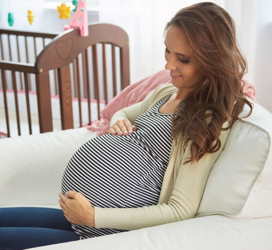 A woman sitting on the couch holding her pregnant belly.