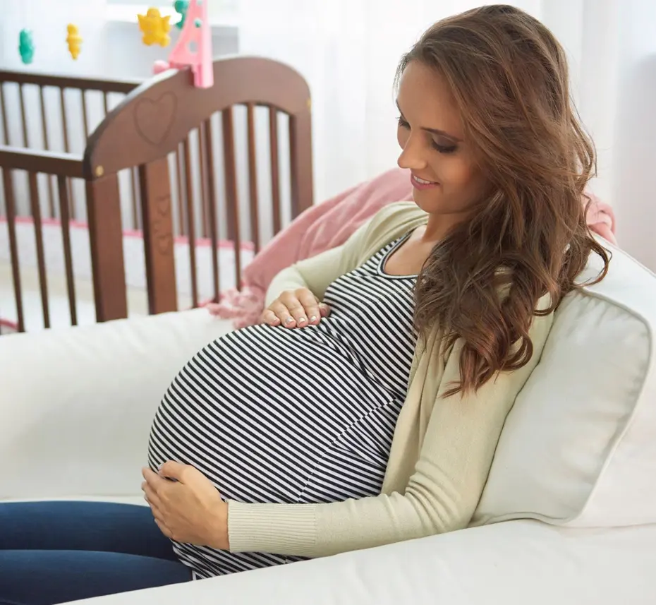 A woman sitting on the couch holding her pregnant belly.